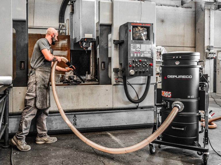 Operator using Depureco M100 industrial vacuum to clean CNC machine area