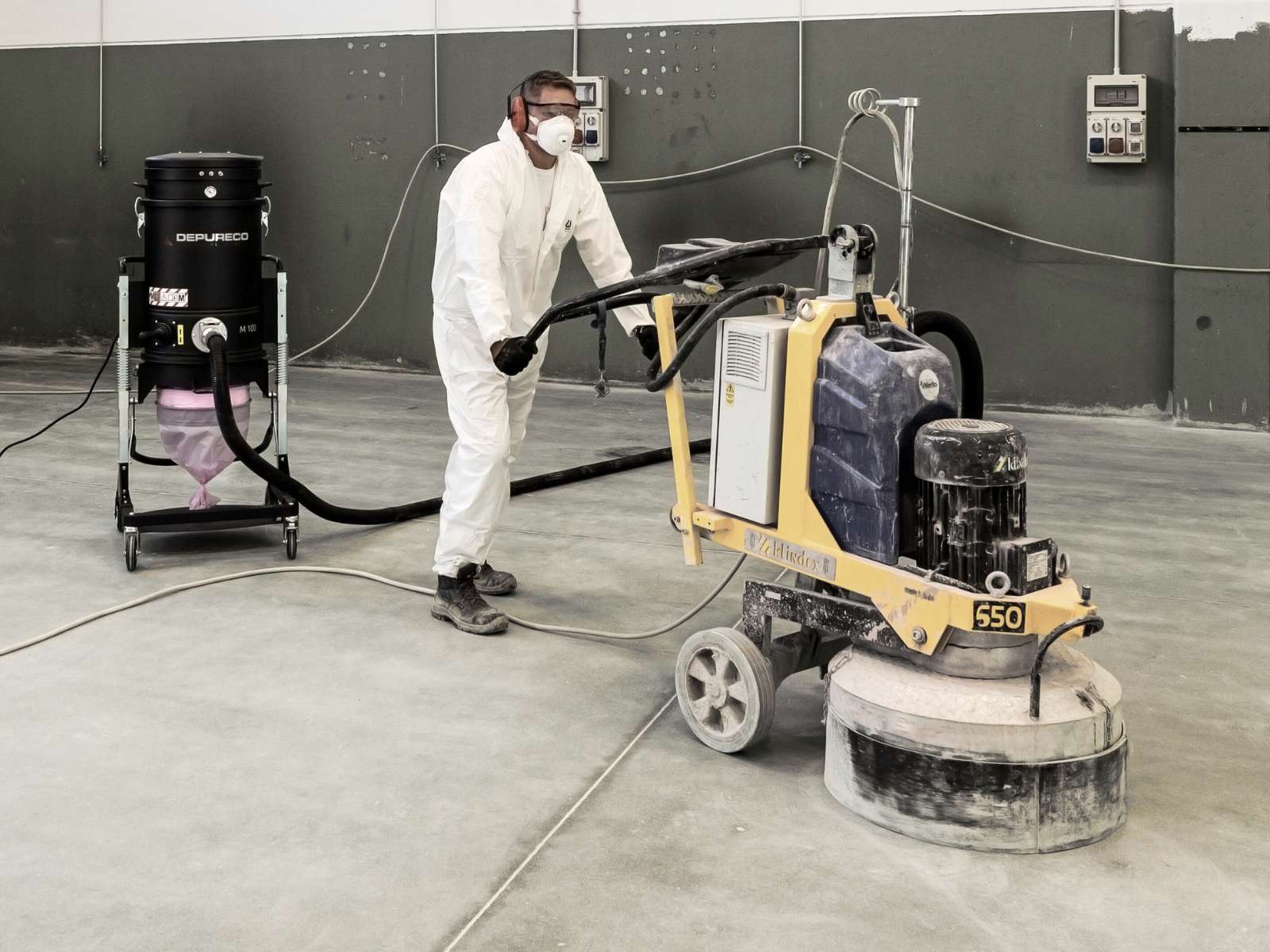 Worker using floor grinder connected to Depureco industrial vacuum for concrete dust extraction