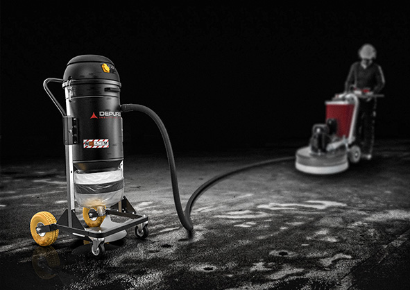 Depureco dust extractor with continuous liner bag connected by hose to a concrete floor grinder during wet/slurry cleanup.