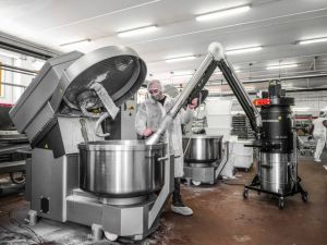 Technician using an extraction arm and mobile dust collector at a large dough mixer in a bakery.