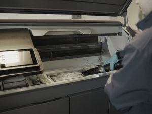 Technician vacuuming residual powder inside a powder-bed fusion 3D printer build chamber.