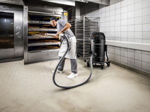 Worker cleaning bakery floor using Depureco industrial vacuum near ovens