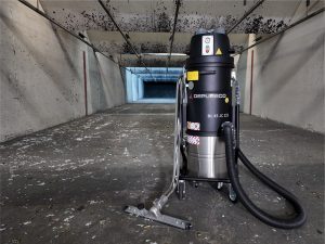 Depureco BL45 JC Z22 industrial vacuum cleaner with S-pipe and floor brush attachment in an indoor shooting range lane, designed for dangerous dust, brass, and target paper cleanup.